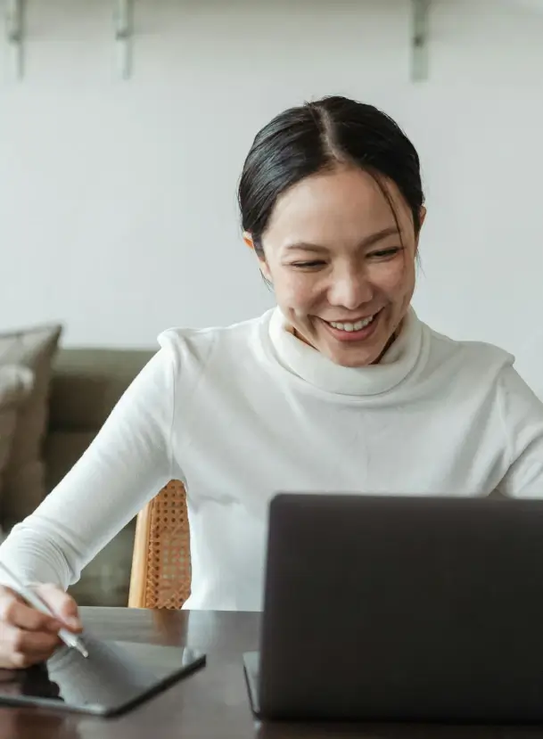 photo of woman looking at laptop and writing things down