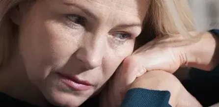 A close-up portrait of an adult with light-colored hair resting their head on one hand, gazing downward with a contemplative expression.