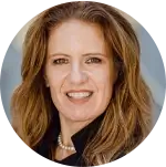 A close-up portrait of a person with long, wavy brown hair wearing a black outfit and a pearl necklace.