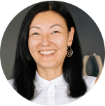 A person with long black hair wearing a white collared shirt and spiral-shaped earrings, framed in a circular crop.